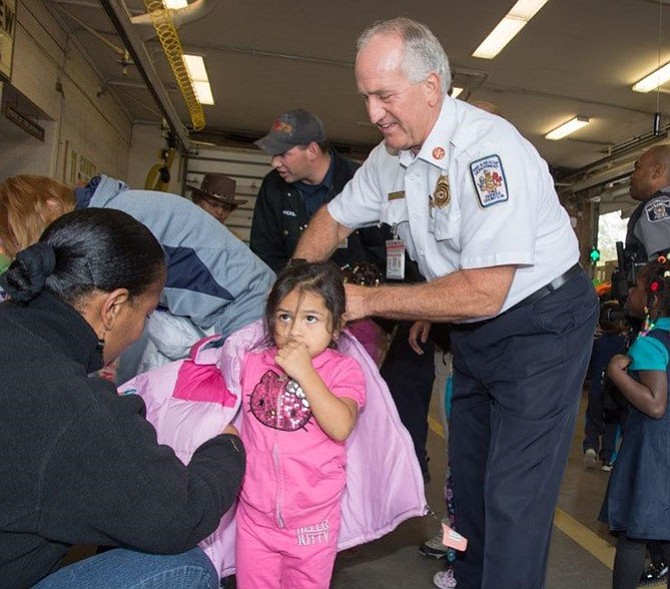 Fairfax County Fire Chief Richard  Bowers helps a child with a coat during the Firefighters and Friends annual coat distribution day Oct. 27 at Penn Daw Station 11. More than 1,600 new coats and over 500 new books were distributed to 70 schools, shelters and nonprofits in Fairfax County and Alexandria.