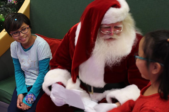 Althea Miedzinski, 9 (left), and her sister Zaira Miedzinski, 7 (right), show Santa Claus their wish list.
