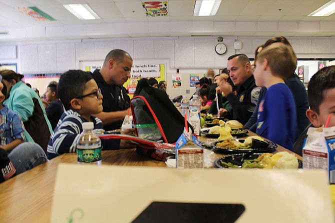 Herndon Police Department Senior Police Officer Ismael Narvaez (center, left) sits across Sgt. Sean Merritt (center, right) to eat lunch with a table full of first grade students.
