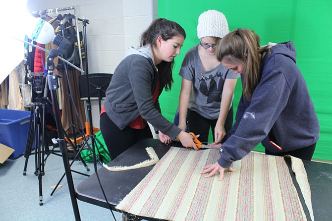 Junior Sarah McDonald, 16 (left), freshman Maddy Rubin, 14 (middle), and junior Amelia Patton, 16 (right), cut fabric to reupholster the seats of chairs used in the show.
