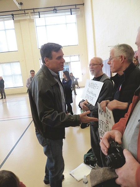 U.S. Sen. Mark Warner tries to shake hands with protesters, agreeing to “negotiate” for fair drug prices.