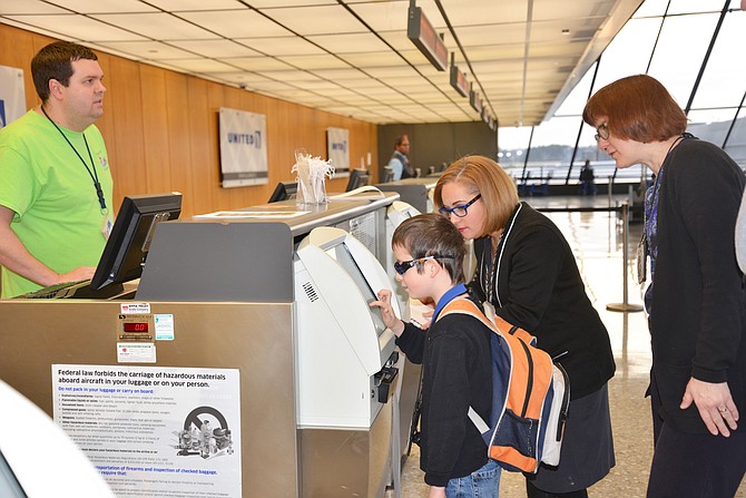 United Airlines employees May Hester and Jeff Lattea assist Felix Reges and mom Ina Laemmerzahl of Reston to “check-in” to their “Wings for All” simulated flight travel experience at Dulles International Airport.
