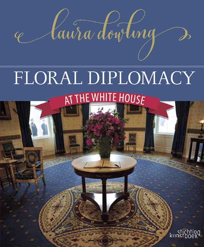 Floral Diplomacy book cover image representing the morning of the official state dinner for India on Nov. 24, 2009, a large display of fuchsia and purple flowers in a decorated lemon leaf creates a colorful focal point in the Blue Room of the White House. 