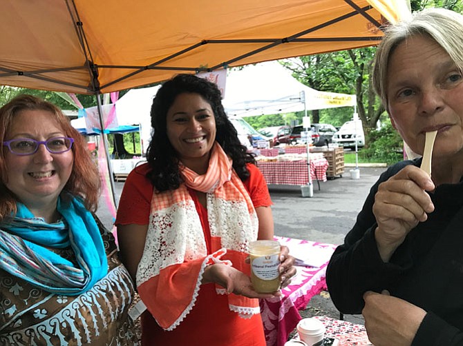 During a pause in sales at the Mclean Farmers Market on Friday, May 12, Andrea Young, fellow vendor and owner of Hidden Creek Farm in Delaplane, Va., sampled Om Lassi's Artisanal Peanut Butter from Susan Sather and Radhika Murari co-owners of Om Lassi in Reston. 