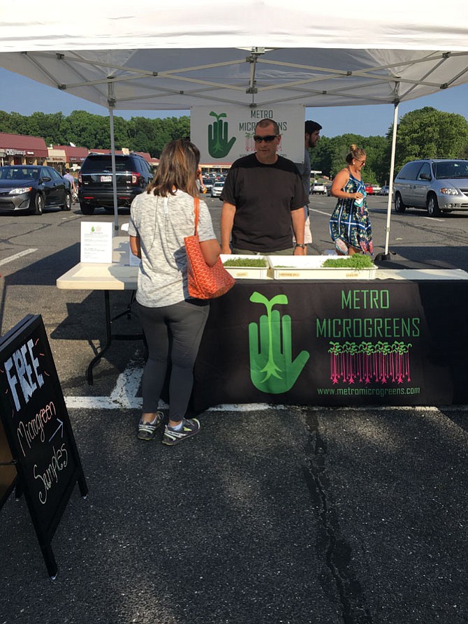 Mark Ross of Metro Microgreens explains his products to a customer at Cabin John Shopping Center Farmers Market, which opened on Thursday.