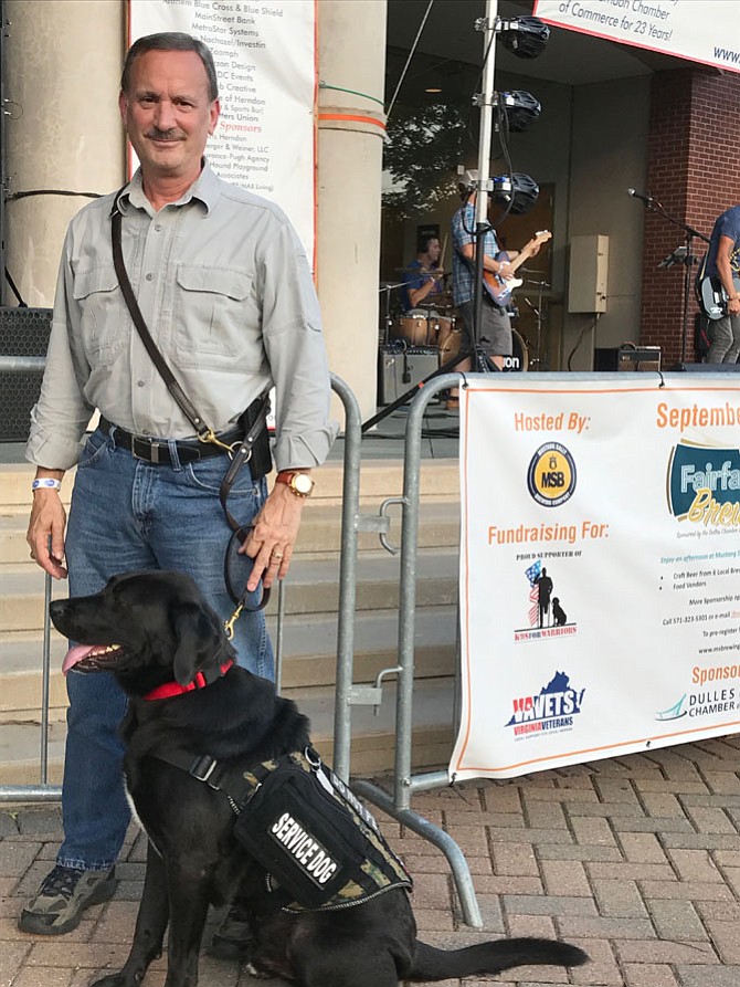 Retired Marine Corps Sgt. Major Jim Kuiken of Vienna and his service dog, Freedom stand next to the Friday Night Live! banner with the K9s For Warriors logo. Kuiken accepted a $1,000 donation on behalf of K9s For Warriors from Doug Downer at the FNL! concert held July 7.