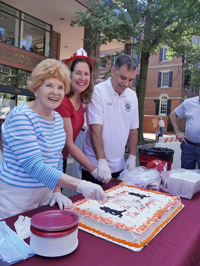 Councilwoman Del Pepper, Mayor Allison Silberberg and Alexandria Fire Chief Robert C. Dubé are ready to cut the first piece of cake at the 243rd birthday party of the Friendship Firehouse Festival. This is sponsored by the Friendship Veterans Fire Engine Association. Pepper said, “This is sure a large knife.”