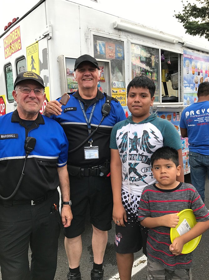 Kevin Garcia, 12, of the Town of Herndon and his brother Fernando, 6, talk with Herndon Police Department Civil Volunteers Steve Marshall and Fred Kibler. Asked what they what they want to be when they grow up, Kevin quickly responds a lawyer, but Fernando quietly says, “Quiero ser policia. Son mis amigos."
