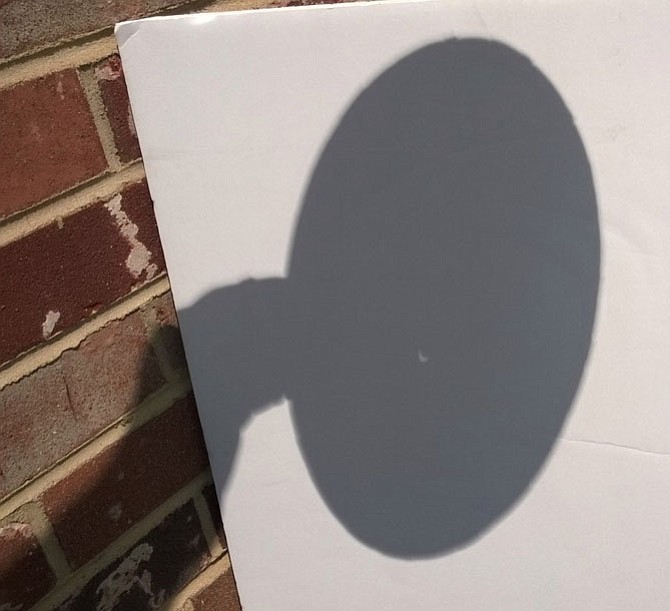 Partial solar eclipse seen at 2:22 p.m. Monday, Aug. 21 in the City of Fairfax through a crude pinhole viewer made by the photographer with a paper plate pierced by a nail and a screen fashioned from a foam presentation board.  The white crescent of sunlight not blocked by the shadow of the moon resembles the tip of a fingernail. 