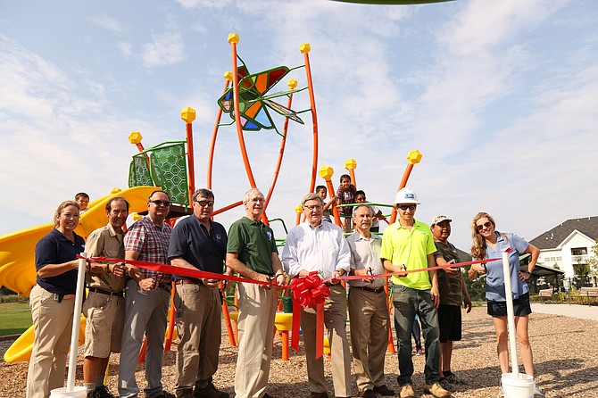 A ribbon-cutting ceremony was held on Saturday, July 22, to mark the completion of the new park. Front row, from left: Fairfax County Park Authority Deputy Director and Acting Executive Director Sara Baldwin; Maintenance Crewmember Rob Aaront; Planning and Development Director Dave Bowden; Area 6 Manager Wayne Brissey; Dranesville District Representative to the Park Authority Board Tim Hackman; Dranesville District Supervisor John Foust; Urban Limited Director of Landscape Architecture Kevin Tankersley; CBG Building Company Project Engineer Jake Bronstein; Herndon Resident Davison Benton; and Greystar Community Manager Catherine Hughes. Back row, from left: Aiden Buche, 4 (on slide); Davison Benton Jr., 8; Justice Benton, 9; Davison Benton, 12; and Danika Benton, 4 (unseen standing behind her father).