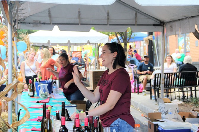 Sara Davenport of Twisted Vines Bottleshop & Bistro waves to a customer sampling the stores' wine selection at the Fall Fest.
