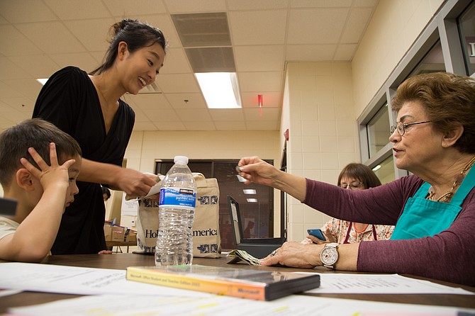 From left: Jayoung Han, a McLean resident and stay-at-home mom, and her son Henry checkout children’s books from Elaine Lailas of Leesburg, a 50-year member of the AAUW at Spring Hill Recreation Center Friday, Oct. 6.