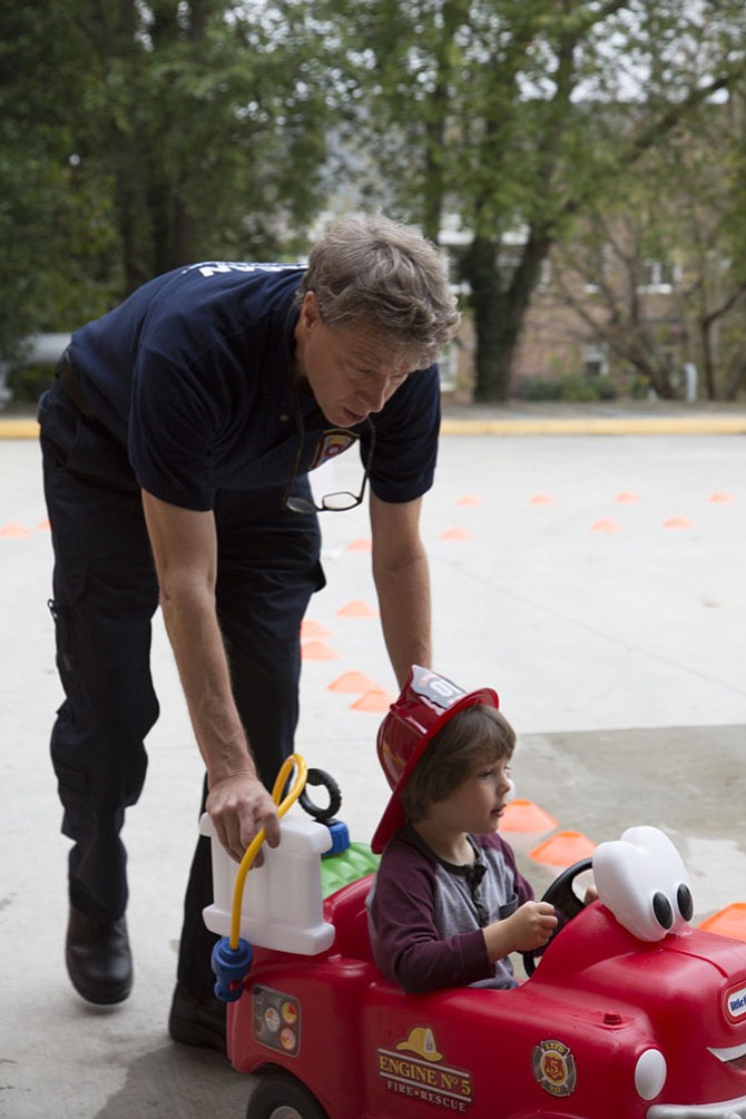 Mac Reed of McLean, a volunteer emergency medical technician with the McLean Volunteer Fire Department, pushes Kameron Kruse, 3, of McLean through a driving course on a 22-inch tall Little Tikes “Spray & Rescue Fire Truck,” complete with a pressurized water tank and hose to squirt water onto a pretend fire at the end of the course.
