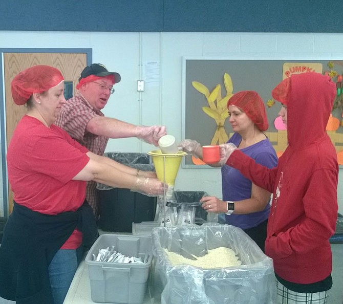 Burke residents Anne and Dave Leeson, left, and Amy and Joseph Baldi, right, fill a plastic bag Oct. 21 with a vitamin pack, a scoop of soy flour, a tablespoon of dehydrated vegetables and a scoop of rice in the cafeteria at Terra Centre Elementary School on Burke Centre Parkway for hunger-relief charity Rise Against Hunger. 
