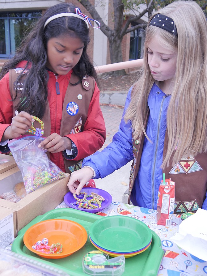 Chocolate frosted, glazed and custard-filled donuts sit on the table at the Central Library for hungry voters. Lizzie Neale (right) of Brownie Troop 6880 says the money will go for military activities and to help their troop. Meera Kuma has also made bracelets. Meera says these will sell for $2 because they take 2-3 hours to make.