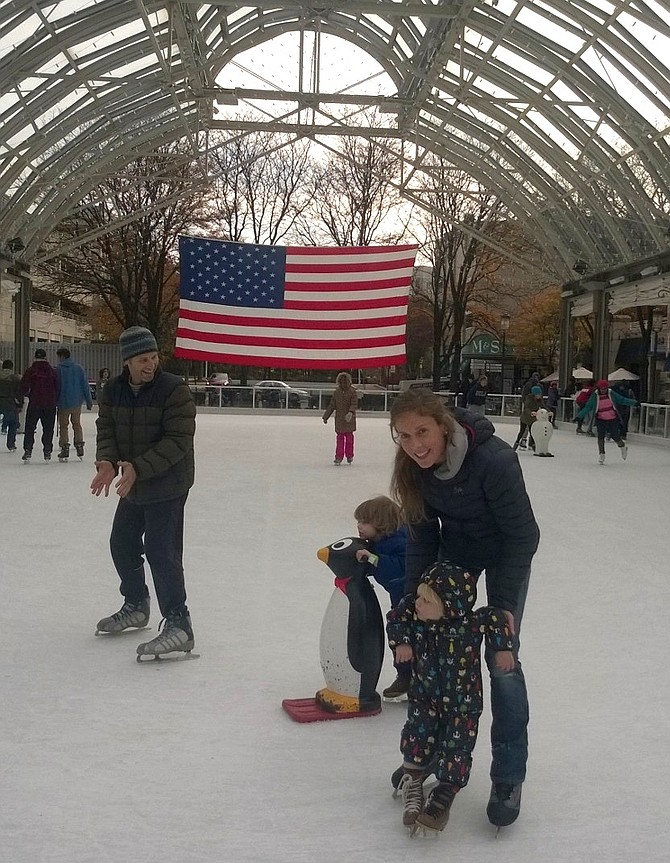 Ryan McKinney, left, applauds his 3-year-old son, Bryce, Sunday afternoon at the Reston Town Center pavilion. His wife, Jessie McKinney, right, holds onto their other toddler, Finn, so his feet can get used to the slick surface. Both parents admit it’s a blast teaching their kids how to skate for the first time Nov. 12. This particular rink holds a special place in their hearts. “We went on our first date here when we were 15 years old,” says Ryan, 38. 