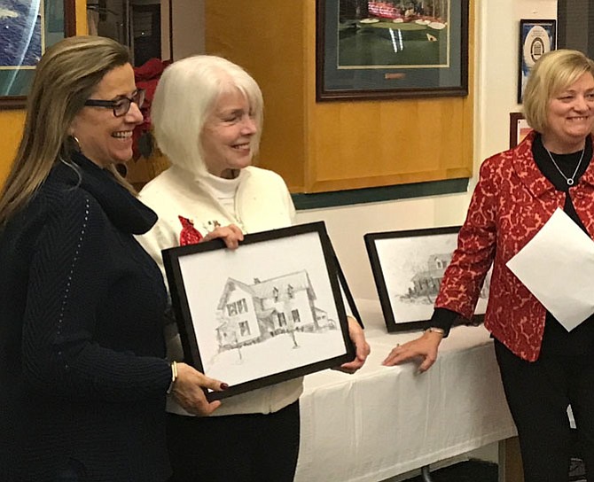 Patti Kelly, owner of 106 Monroe Hill Court accepts the pen and ink drawing of her home created by local artist Pat Macintyre during the reception held for the five homeowners whose properties were featured on The 2017 Holiday Homes Tour of Herndon. Homes Tour committee Co-chair, Susan Anselene looks on.