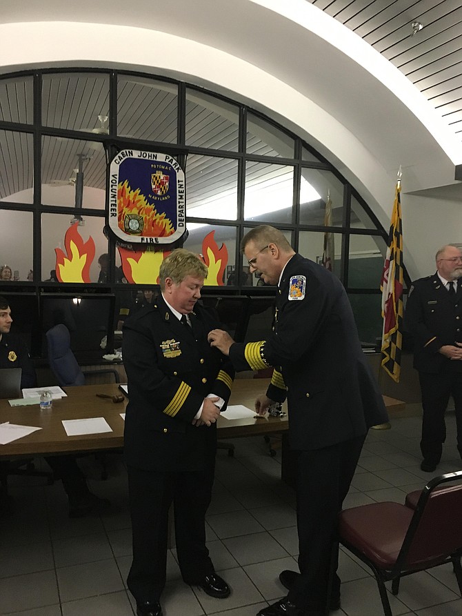 Retired Chief James Seavey pins the chief’s badge on Corinne Piccardi, who was sworn in as new head of the Cabin John Park Volunteer Fire Department on Monday, Jan. 22.