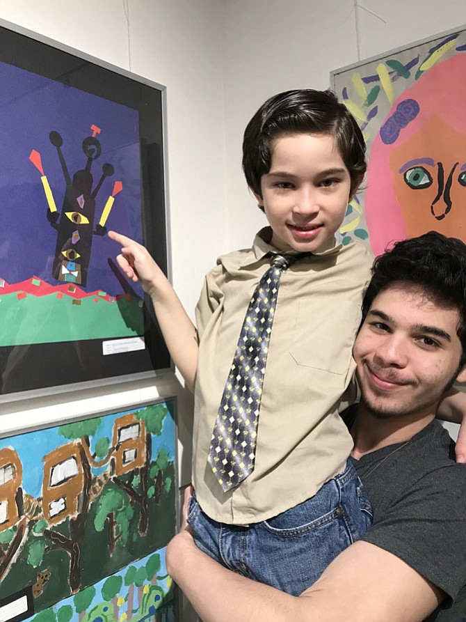 Gabriel de Moraes, 8, a second-grader at Dogwood Elementary, gets a lift up by big brother Igor so he can point out his collage selected for the exhibition at the Jo Ann Rose Gallery, Reston Community Center Lake Anne, held in celebration of National Youth Art Month.