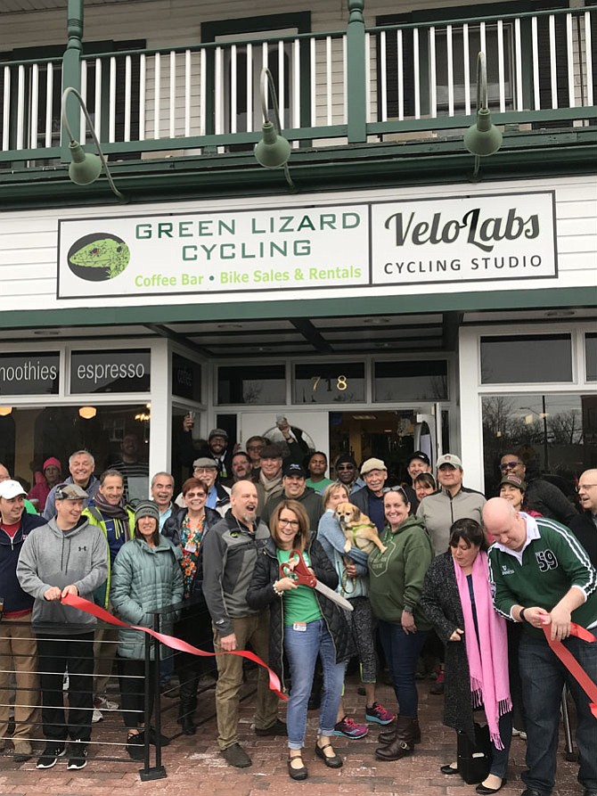 Mayor of Herndon Lisa C. Merkel cuts the red ribbon in celebration of Green Lizard's Fifth Anniversary and signing of a new 5-year lease on the property. Dave Meyer and Beth Meyer, owners of the Lizard, stand on each side of Merkel as patrons and friends gather to join in the festivities.