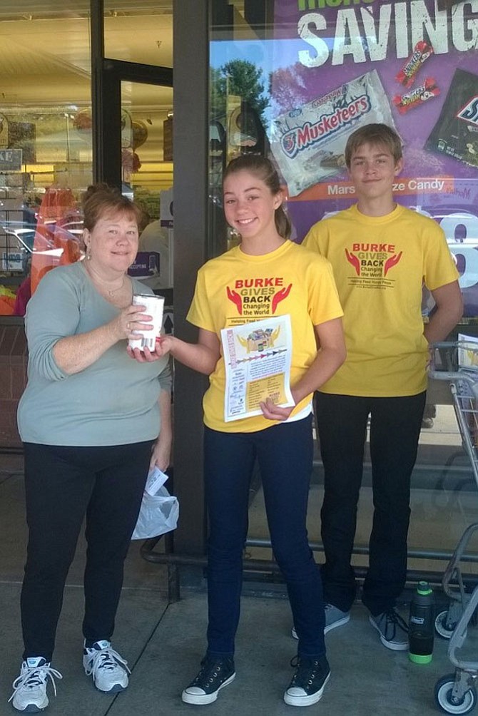 Maggie Waldron of Burke gives a 26-ounce can of chicken noodle soup Oct. 21, 2017 to Chloe Charlesworth, 12, and her brother Spencer, 14, in front of the Giant Food grocery store at the Burke Town Center. The Lake Braddock Secondary School students volunteered last fall for the “Burke Gives Back: Changing the World” teams at three grocery stores along Burke Centre Parkway between Ox and Old Keene Mill roads. Burke residents can shop again at these stores  May 19 from 9 a.m. to 1 p.m. and help keep 400 local children from going hungry this summer in Fairfax County. Grocery lists will be distributed at the entrances of Safeway at 5727 Burke Centre Parkway, Giant Food at 6011 Burke Centre Parkway and the Safeway at 9596 Old Keene Mill Rd. 