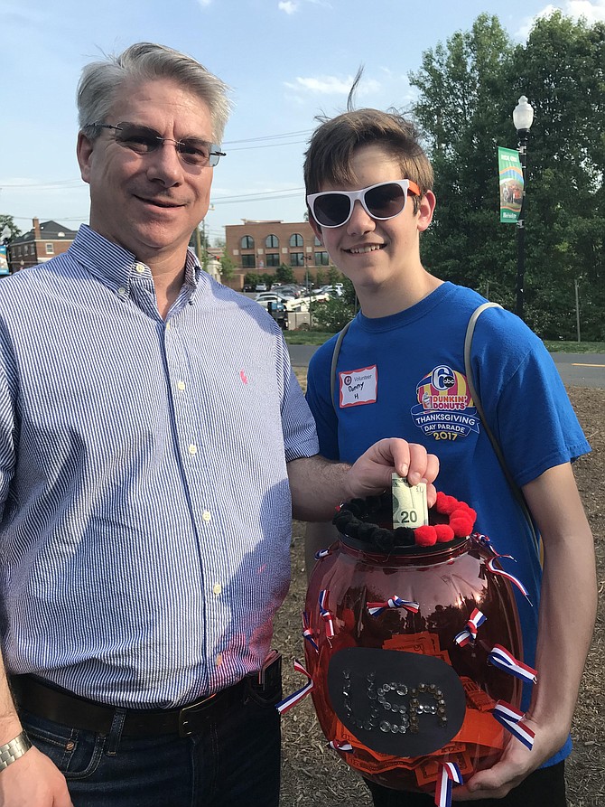 Dion Stempfly drops a donation in the jar held by band member Danny Hale, 15, of Herndon before he enters the Free Normandy Kickoff Celebration and Benefit Concert performed on the Herndon Town Green Saturday night, May 12. Funds raised will help offset expenses for the band to go to Normandy in June 2019.