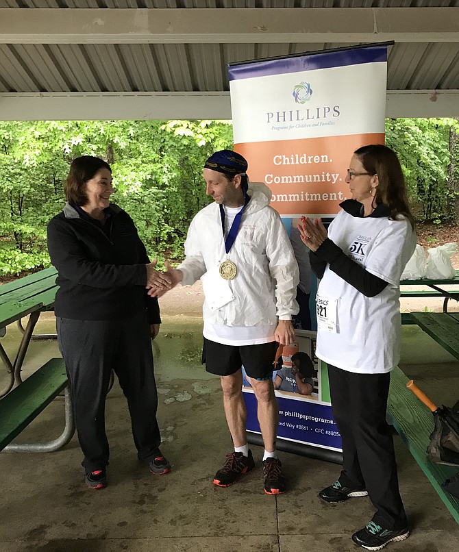 Dennis Billings accepts first place for winning the Phillips organization’s first ever 5K, shaking hands with Director of Development Debi Alexander, from McLean.