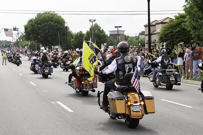 Many motorcycle riders wave flags to remember the fallen as crowds cheer them on.