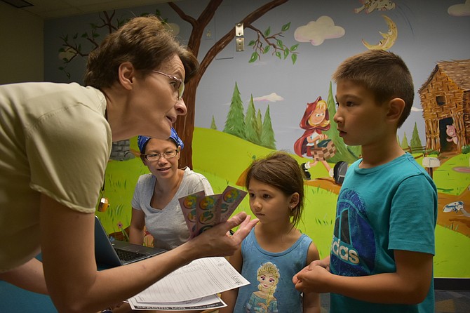 Youth Services Manager Dorota Rodgers gives summer reading logs to Alina Brusgul, 4, and Nico Brusgul, 8, at Reston Regional Library.