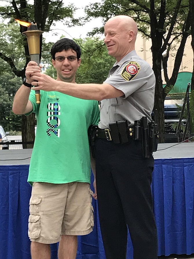 At the inaugural Law Enforcement Torch Run for Special Olympics Virginia at Reston Town Center held on Saturday, July 21, 2018, athlete Joey Wheeler of Lorton accepts the Flame of Hope from Colonel Edwin C. Roessler Jr., Chief of Police, Fairfax County Police Department, before the start of the run. 