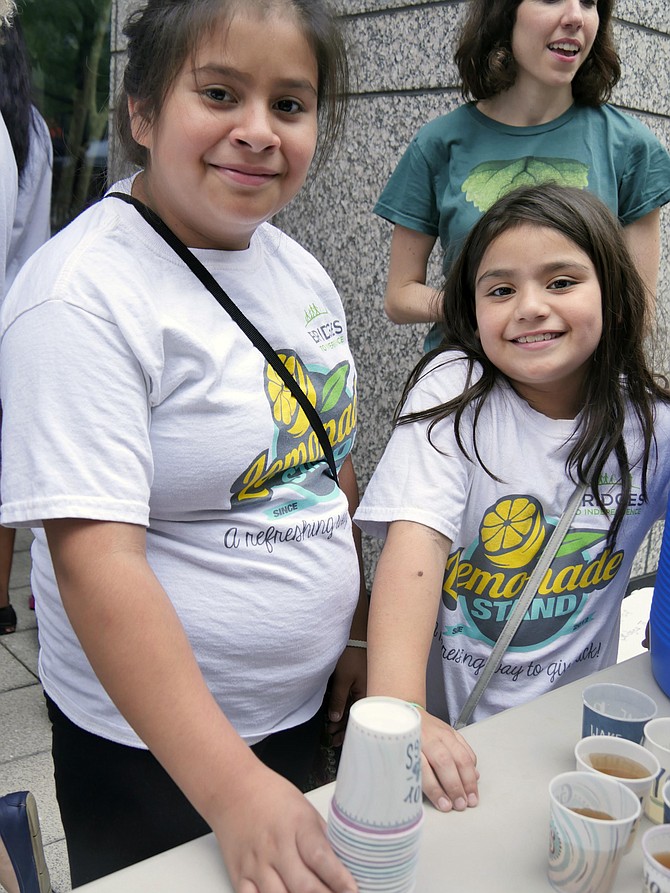 Ten-year-old Brittaney Medina and her eight-year-old sister, Mia, serve cups of lemonade at the Bridges to Independence stand on Aug. 2 at FARMFRESH at Ballston Market.