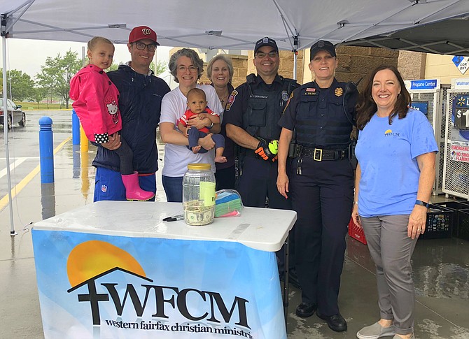 Volunteers braving the rain at the Chantilly Walmart are (from left) Elizabeth Casteel, Andrew Casteel (WFCM Board President), Rebecca Kolowe (WFCM Executive Director) holding baby Triston, Pastor Lynn Miller (WFCM Board member, King of Kings Lutheran Church), APO Nelson Fernandez, APO Ashleigh Soloff and Jennie Bush (WFCM Community Outreach Manager).