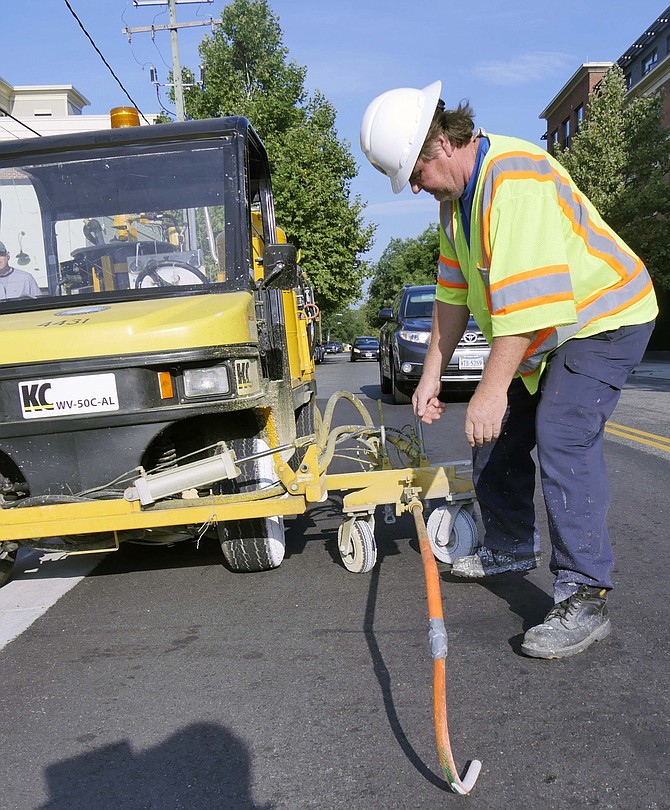 Eddie Billmyer lines up the guide steel rod so he can accurately paint skiff lines on Madison Street in Alexandria.