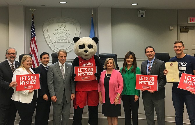 Celebrating Fairfax City’s temporary name change this week to “Mystic City” are (from left) Council members Michael DeMarco, Jennifer Passey and Sang Yi, Mayor David Meyer, Pax the Panda, Council members Janice Miller, So Lim and Jon Stehle and a Mystics representative.