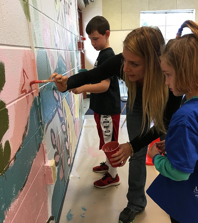 Kaylee Fefferman, 7, watches intently as Artist-in-Residence Sarah Bleiweis demonstrates a brush technique on the giant mural in the Floris School cafeteria being created by K-6th grade students.