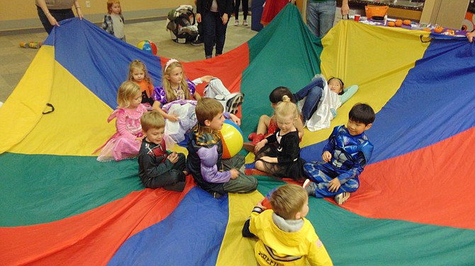 Children play the Popcorn Game with a parachute and beach balls.