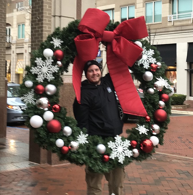 Jimmy Liebro of Choice Planting, Inc. has a little fun with the holiday wreath as his partner adjusts his safety harness before taking the wreath up on the lift and installing it at Reston Town Center.