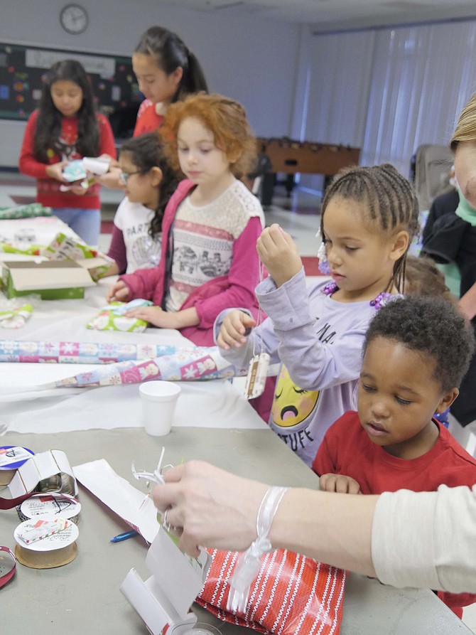 Children line up at the wrapping table clutching a gift to be wrapped by a volunteer for a loved one. One of the volunteers wraps an Elsa Activity book. "We’ve had a lot of these today."