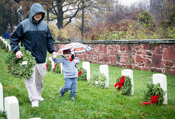 A father and son carry a wreath to place at the grave of a veteran Dec. 15 as part of Wreaths Across America at Alexandria National Cemetery.