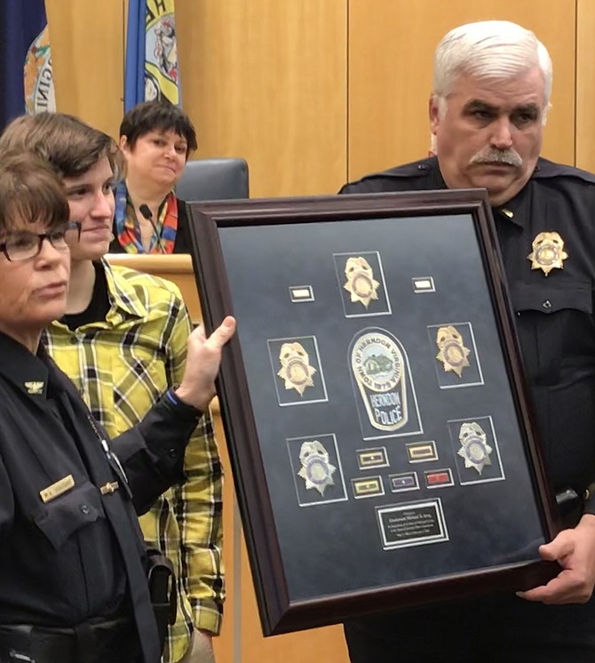 Herndon Police Chief Maggie DeBoard presents Lieutenant Michael "Mike" B. Berg a shadow box with the various valor awards and different badges for his ranks and patches from the Herndon Police Department, with Berg’s family looking on.