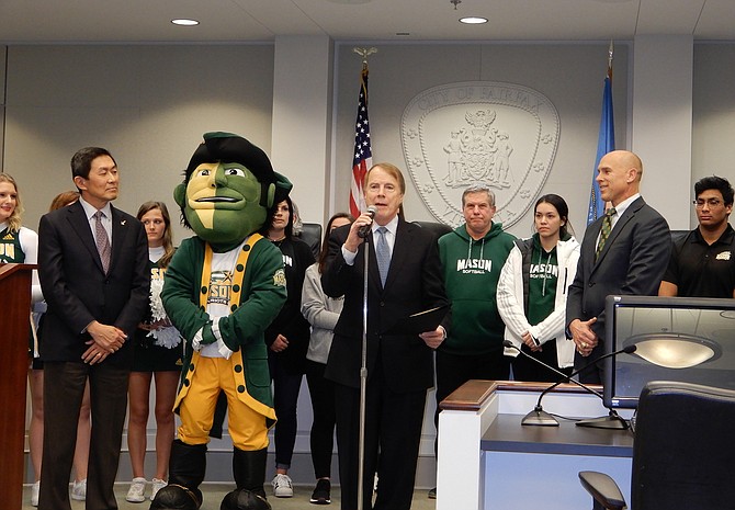 During a City Council meeting, Fairfax Mayor David Meyer (center) declares February as GMU Patriots Month in the City, while the university mascot and representatives look on.