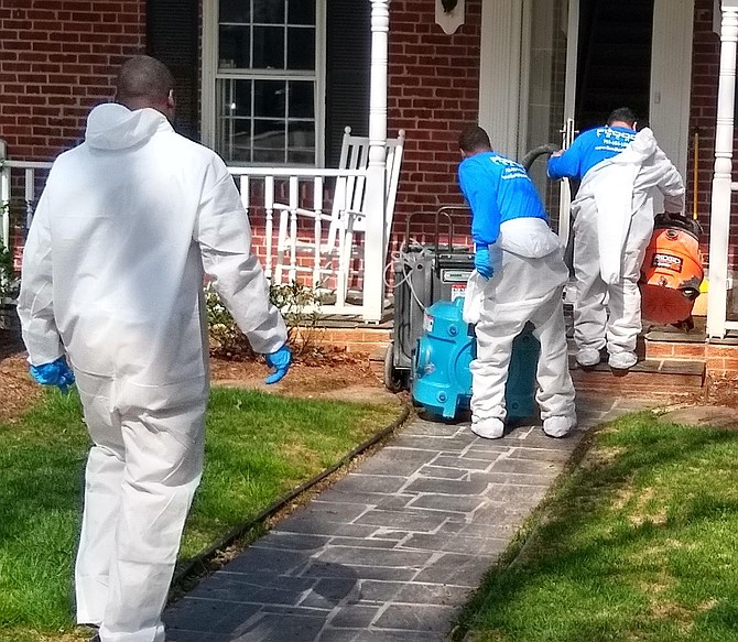 Restoration company employees in “moon suits” arrive to clean out basements filled with sewage from overflow on N. Powhatan Street on April 7.