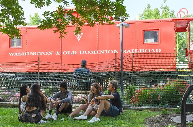 Young adults sit under the shade by the red caboose.