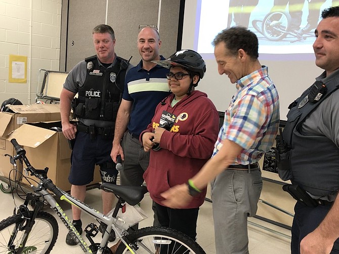 FCPD officers of Reston District station, MPO B.T. McMahon and PFC D. Rocco, along with Raymond Lonnett, Principal, Hutchison ES and Attorney Doug Landau, present Jorge Arce, 12, student at Hutchison Elementary School, with the bicycle he won during Landau Law firm's Lids on Kids program held May 22.