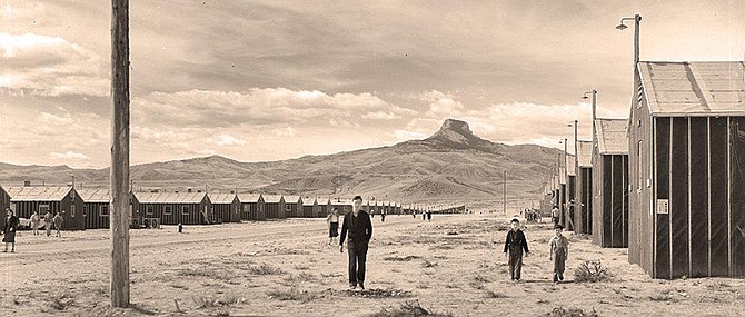 Japanese Americans travel between housing barracks with Heart Mountain on the horizon.