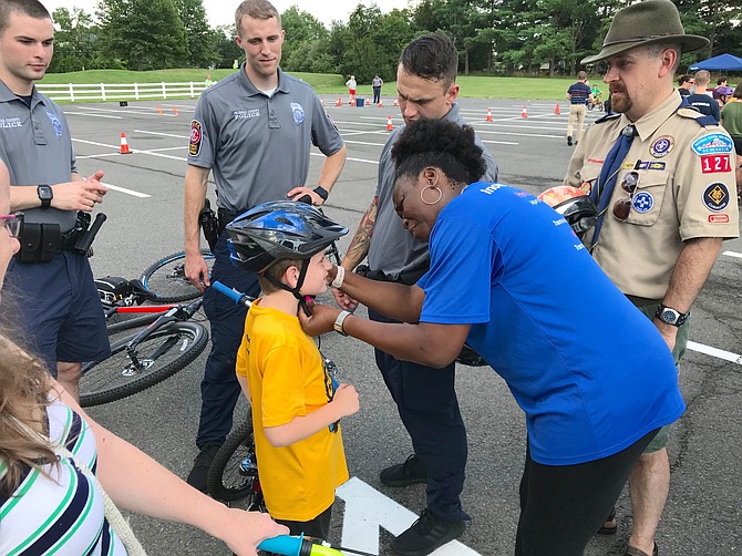 Linda Watkins fits a helmet on a Cub Scout as Bike Rodeo Chairman and cubmaster Kris Keener looks on.