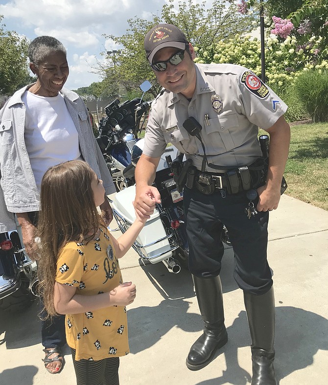 While Supervisor Cathy Hudgins (D-Hunter Mill) looks on, Amirah Khattak, 5, of Reston meets Officer R. B. Kitchens of the FCPD Motor Squad during the 2019 National Night Out celebration hosted by Hunters Woods Neighborhood Coalition and Cornerstones at Hunters Woods Plaza, on Tuesday, Aug. 6.