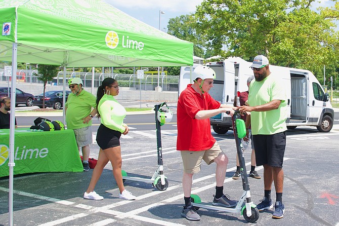 Chad Washington of Lime is instructing Neil Waldman how to operate an electric scooter Saturday, July 27 at the Montgomery County Democracy Boulevard transit site, right near Montgomery Mall.