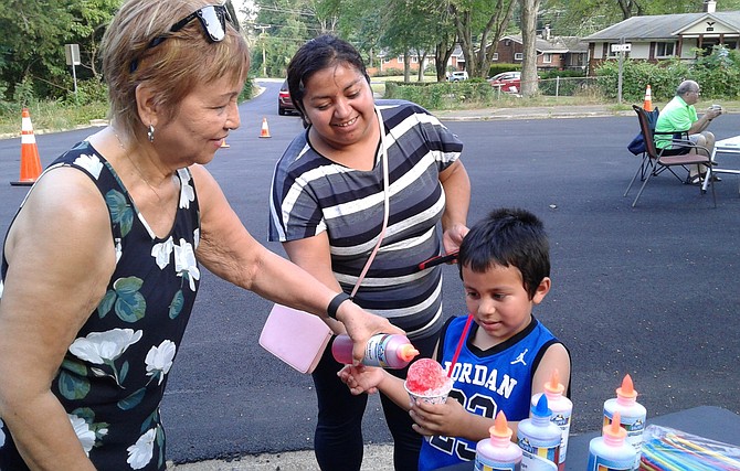 Fleur Noeth, left, adds the finishing touch to the snow cone of Santos Cruz, 5, right, while his mother, Belgica Cruz helps her son stay still for a brief moment Aug. 6 in Alexandria at the Bren Mar community block party during the 35th annual National Night Out.