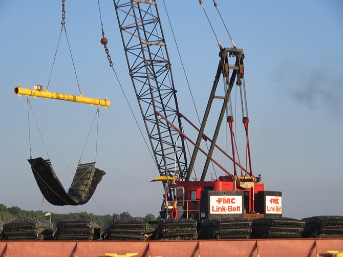 A crane lowers a marine mattress into the river to support the breakwater.